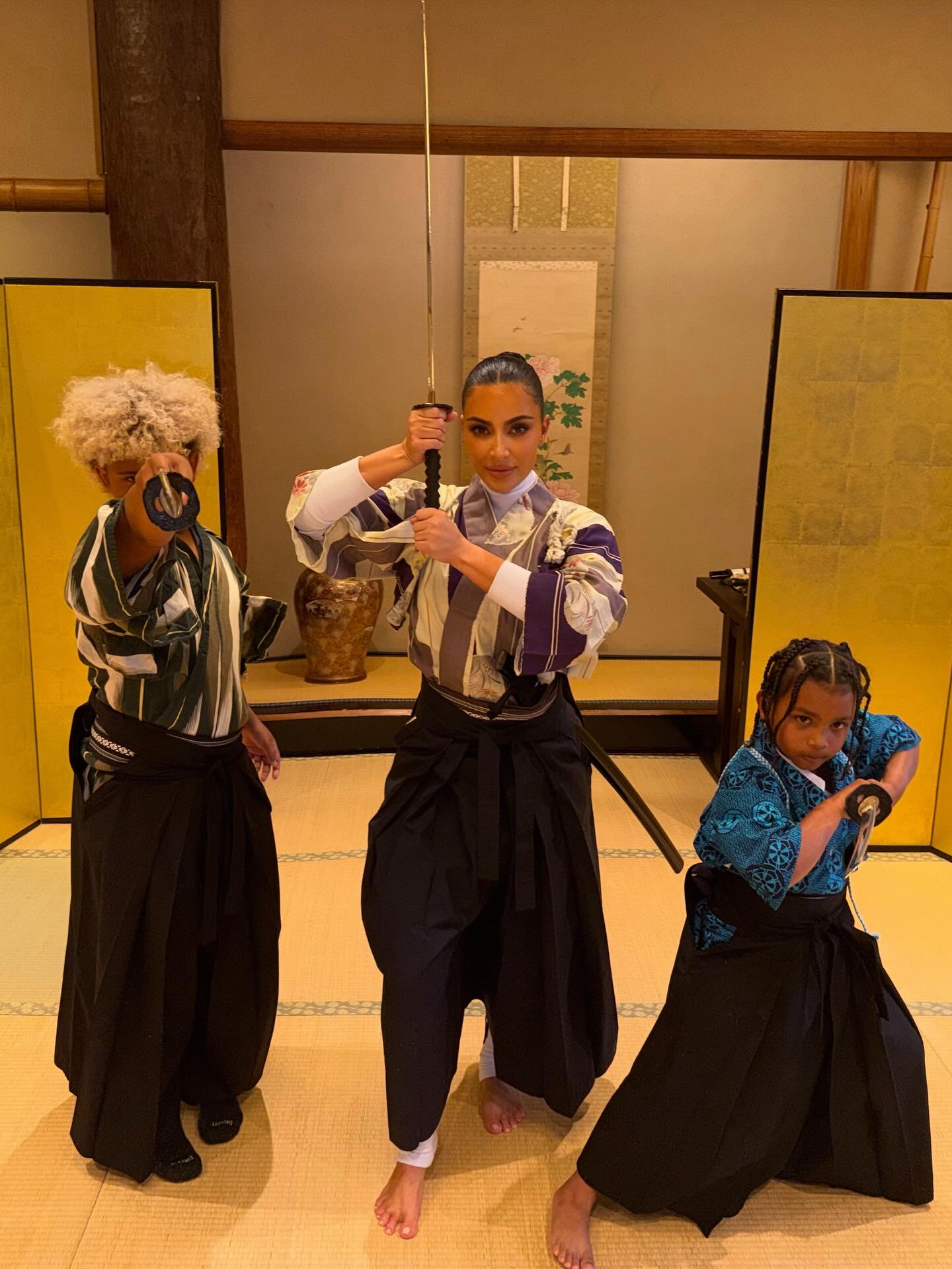Kim Kardashian and her two children in traditional Japanese attire, holding samurai swords.