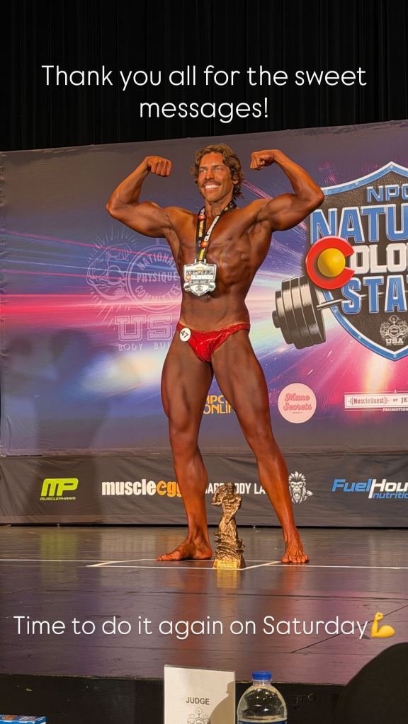Joseph Baena posing on stage at a bodybuilding competition with a medal and trophy.