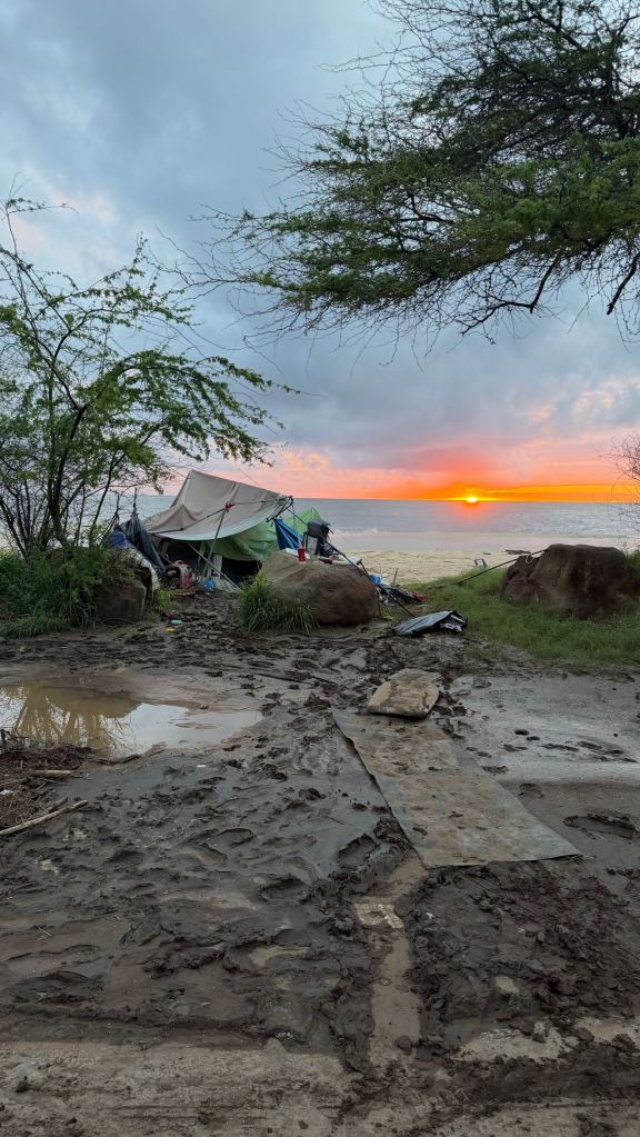 A tent settlement on a muddy beach with a sunset over the ocean.