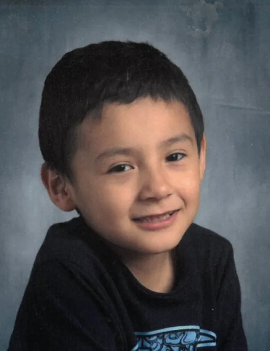 Photo of Remi Stately, a young boy with dark hair and a dark shirt, smiling slightly.