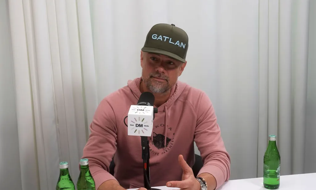 Josh Duhamel speaking into a Dear Media microphone, wearing a pink hoodie and