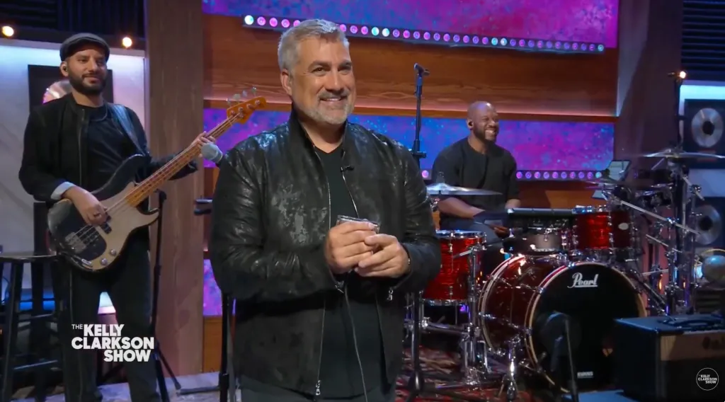 Taylor Hicks smiling and holding a harmonica on The Kelly Clarkson Show.