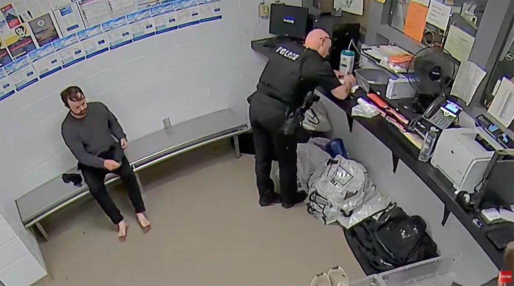 Joseph Duggar stands barefoot while a police officer searches items on a counter.
