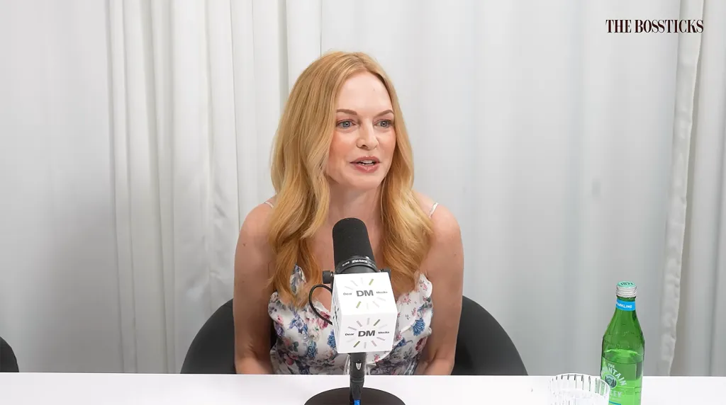 Heather Graham sitting at a table with a microphone in front of her.