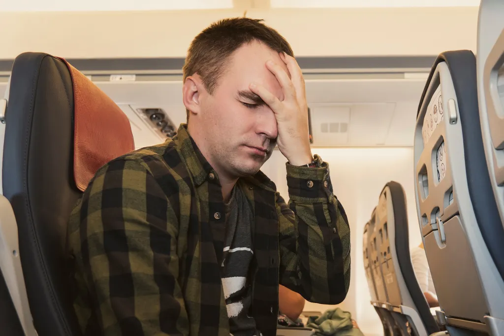 A young man with a headache or aerophobia holding his forehead in an airplane cabin.