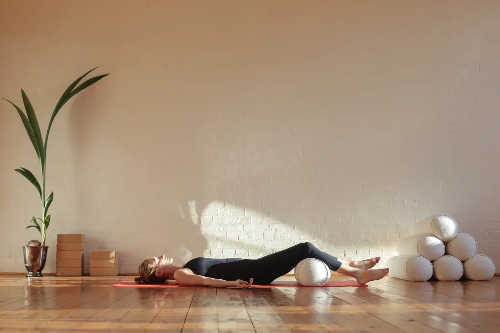 Woman performing a breathing exercise in shavasana on a yoga mat.