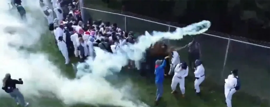 Activists release colored smoke near a fence.