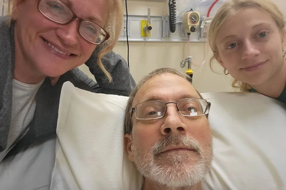Eric Tennant in a hospital bed with his wife, Becky, and daughter, Amiya.