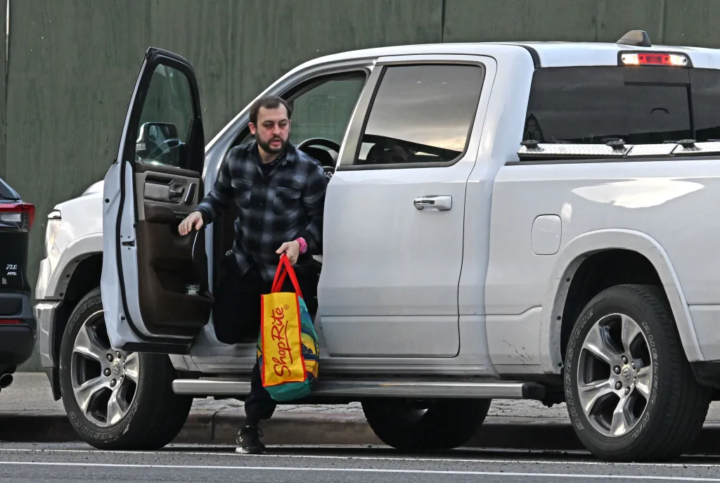 Man in a plaid shirt exiting a white pickup truck, holding a ShopRite reusable bag.