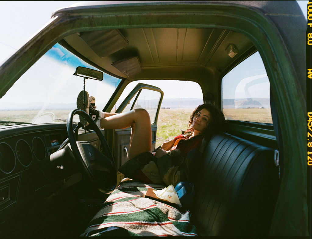 A woman reclines in the driver's seat of a truck, her feet propped on the steering wheel.