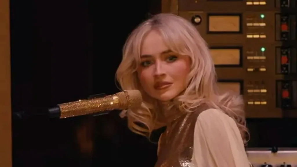 Sabrina Carpenter singing into a gold-glittered microphone.