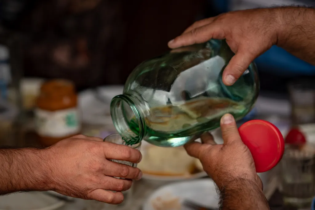 Two hands holding a large glass jar and pouring its contents into a small glass.