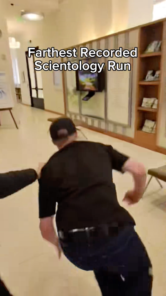 A person wearing a black shirt and dark pants running away from the camera in a building with a title that reads 