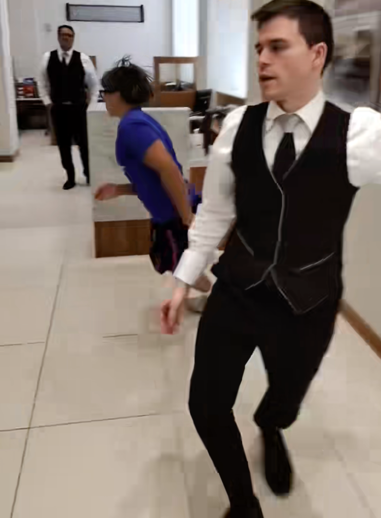 Two men in vests and a person in a blue shirt running through a room.