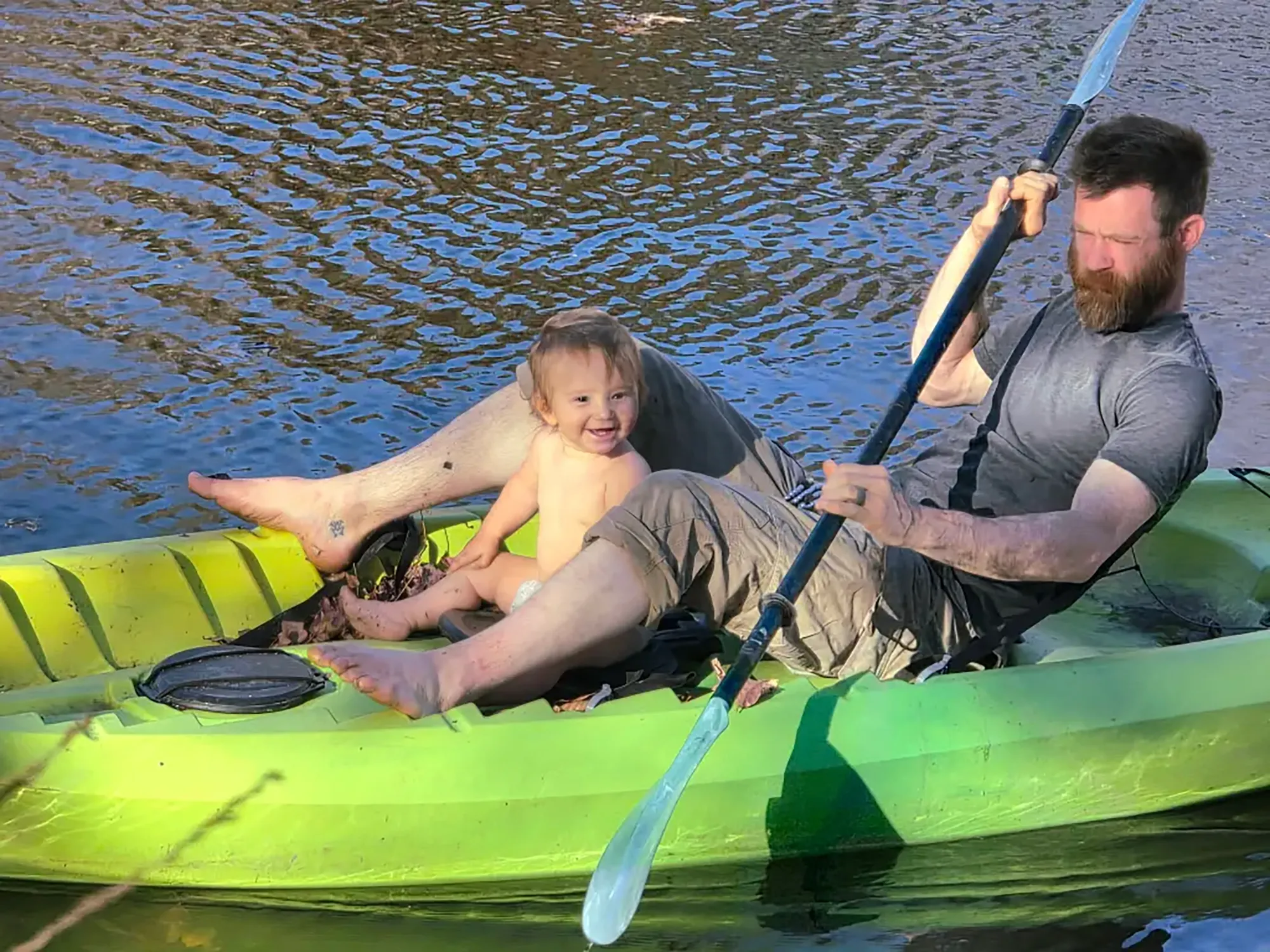 A man with a beard and a young child in a neon green kayak on the water.