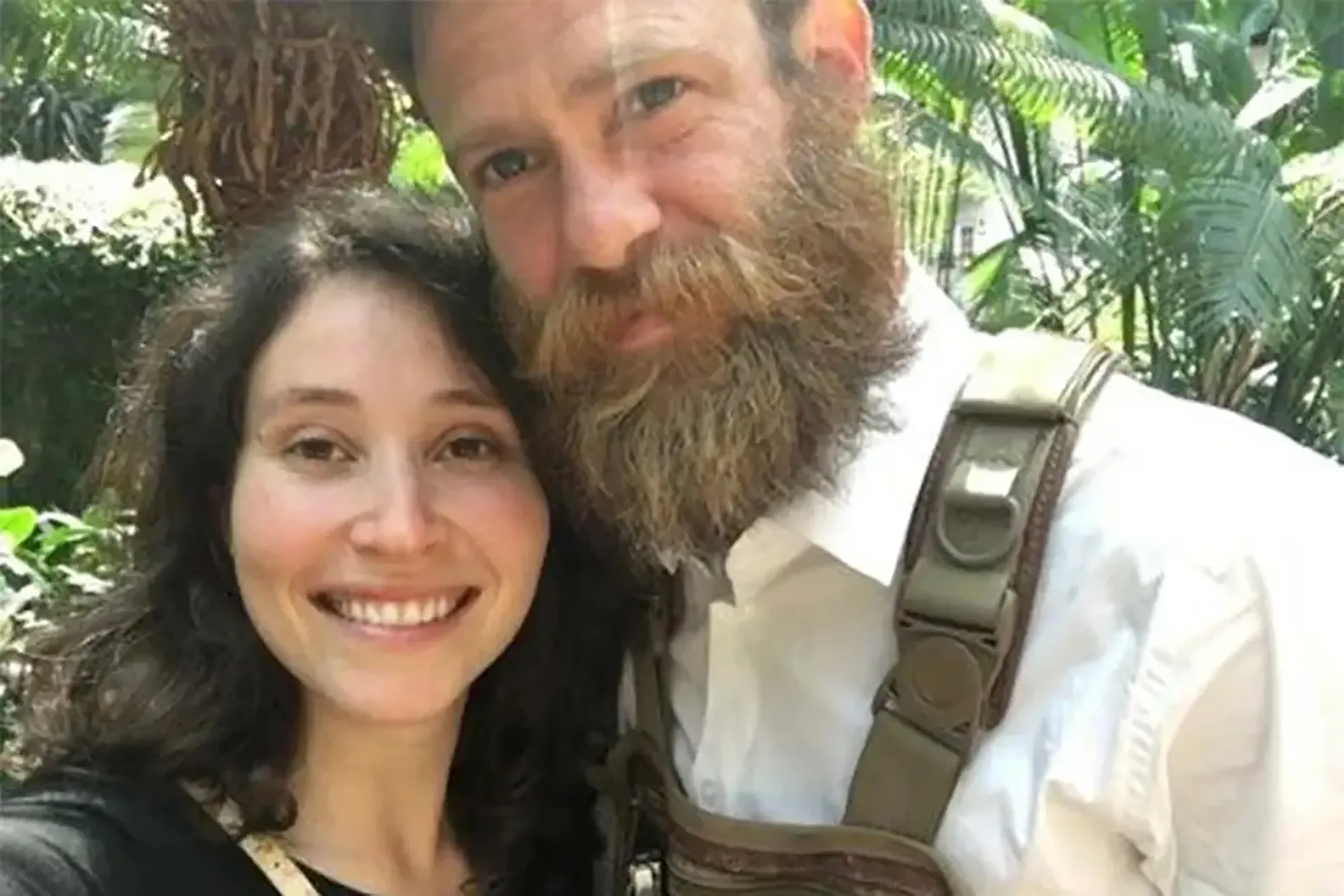 A smiling woman with dark, curly hair and a man with a long beard and white shirt stand close together.
