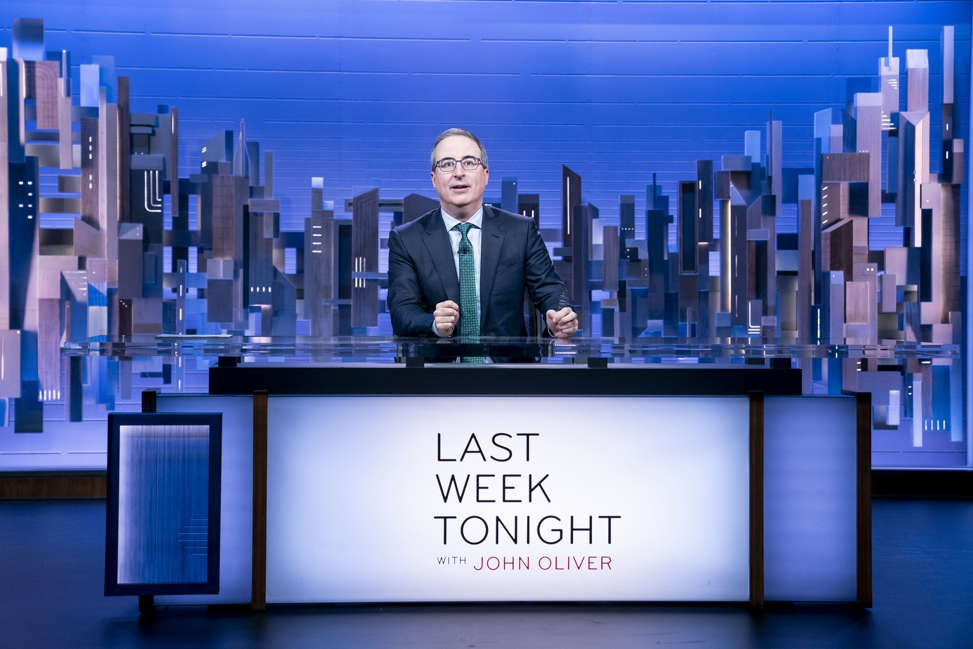 John Oliver standing at a desk with 