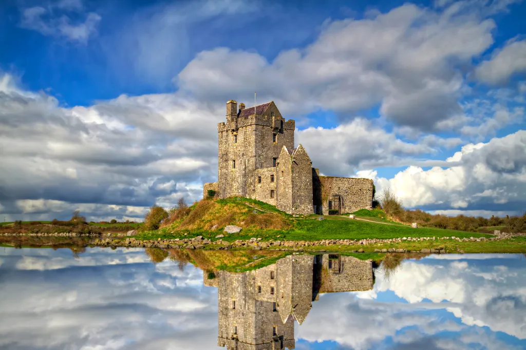 Dunguaire Castle near Kinvarra, County Galway, Ireland, reflecting in still water under a cloudy sky.