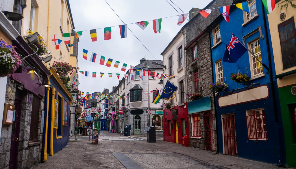 View of the main high street in Galway City with brightly painted buildings and cobblestone streets on a cloudy day.