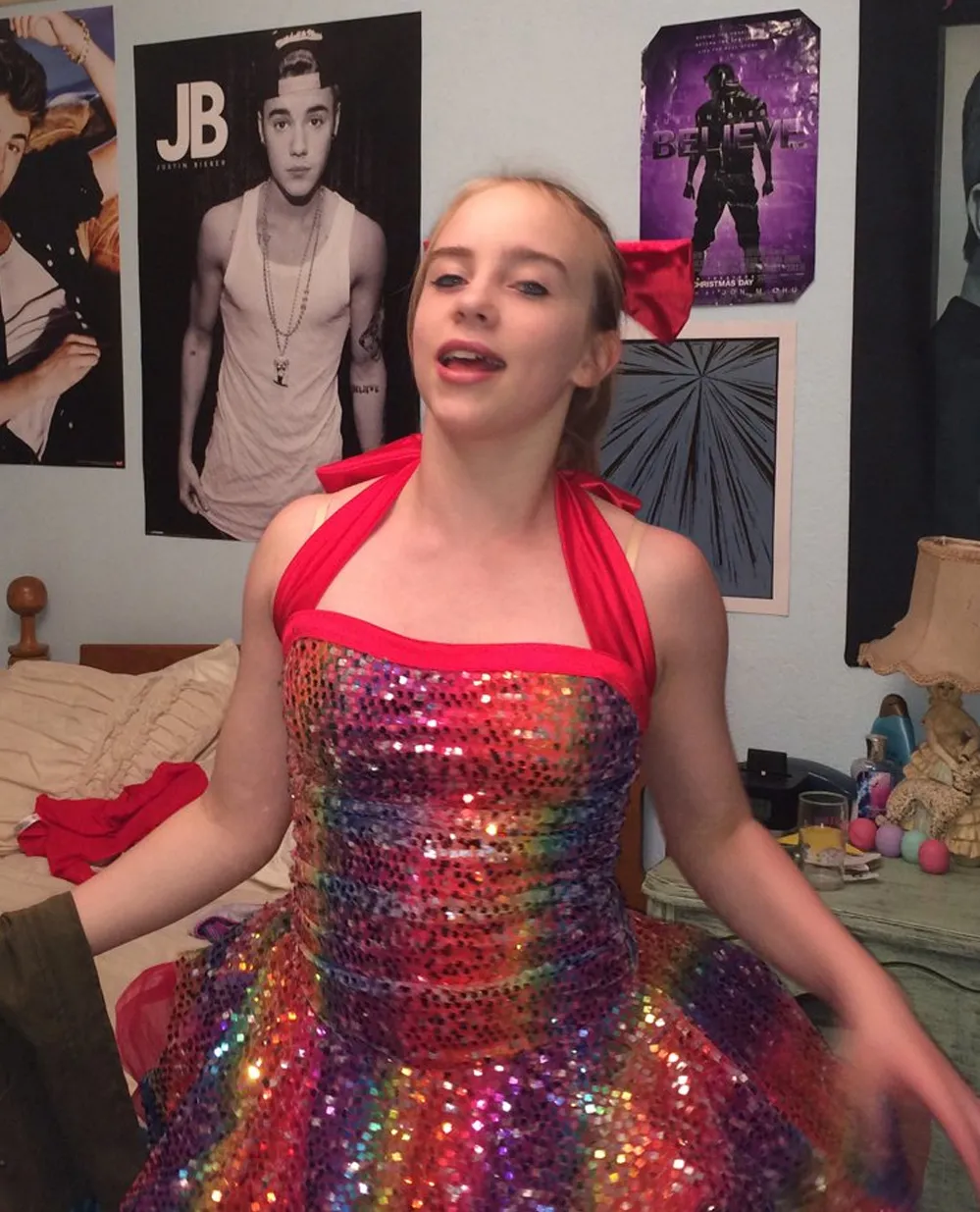 Young Billie Eilish in a rainbow sequined dress with Justin Bieber posters in the background.