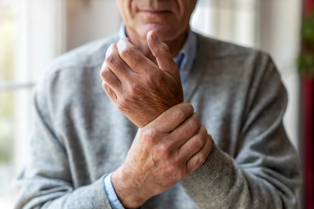 An elderly man with arthritis massaging his wrist.