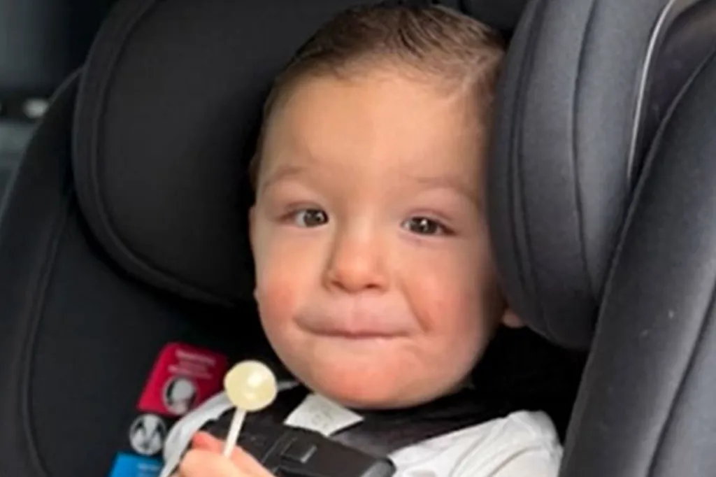 A young child in a car seat, holding a lollipop.