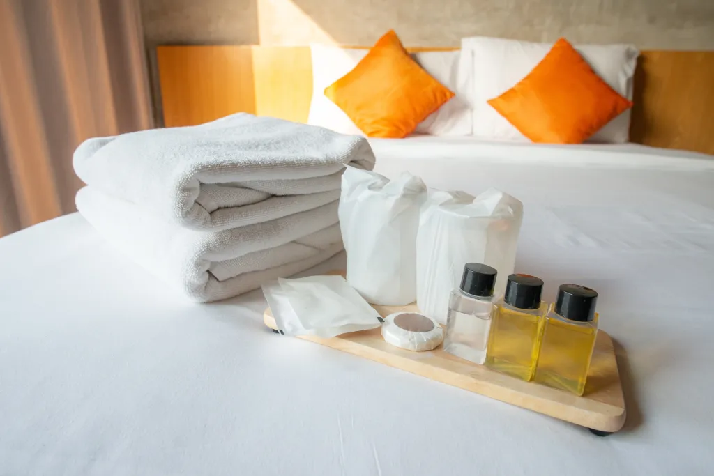 Hotel amenities, including folded towels, soaps, and shampoo bottles, arranged on a bed.