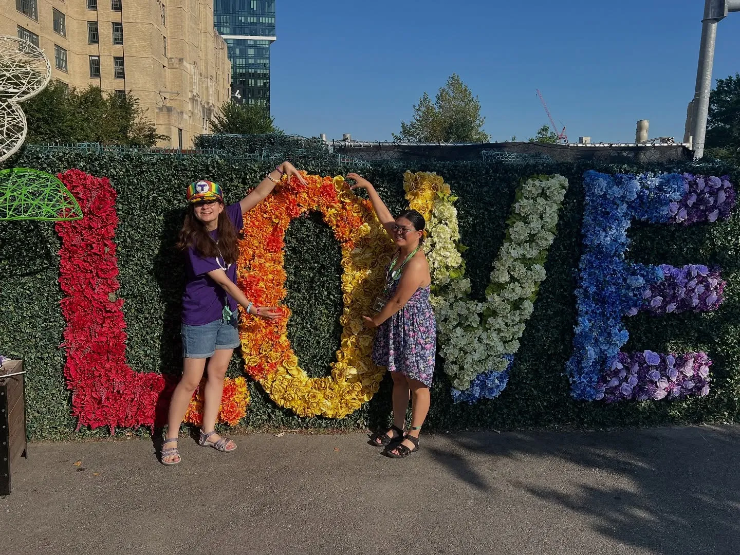 Tina Zhu Xi Caruso and Pari Kim posing in front of a flower display that spells 