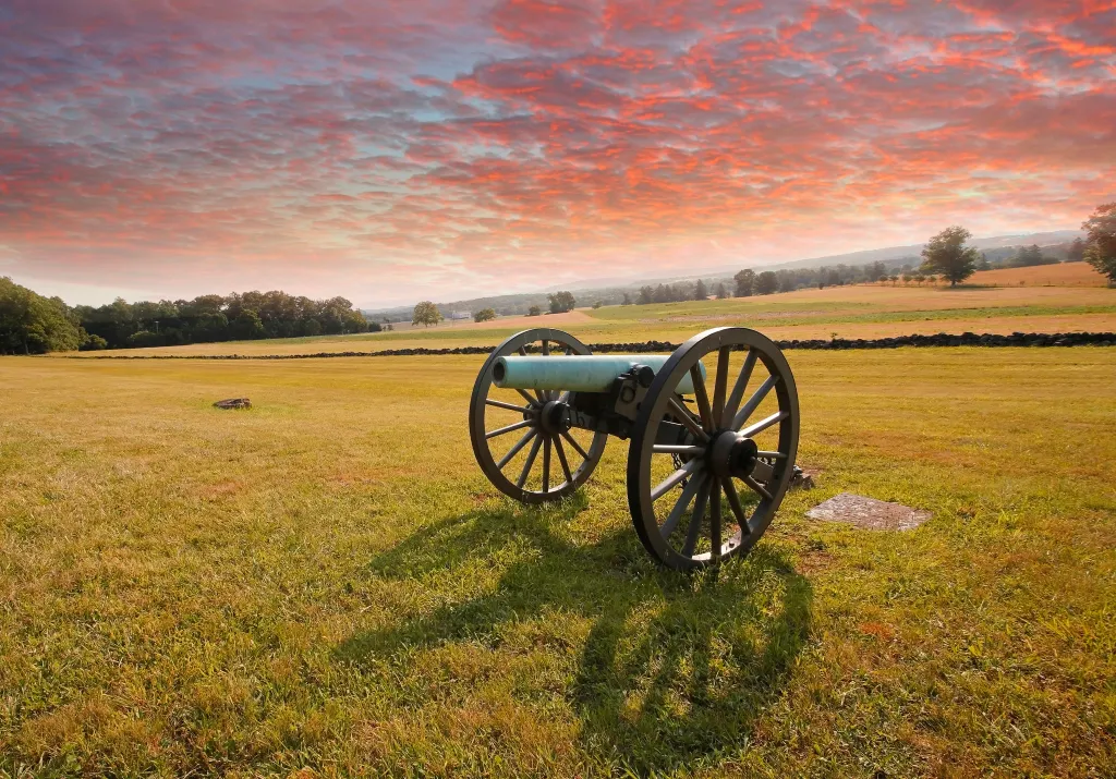 An antique artillery cannon on a grassy battlefield at sunset.
