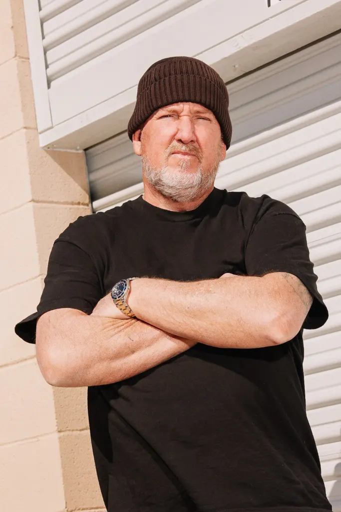 A man with a brown beanie and black shirt standing with his arms crossed.