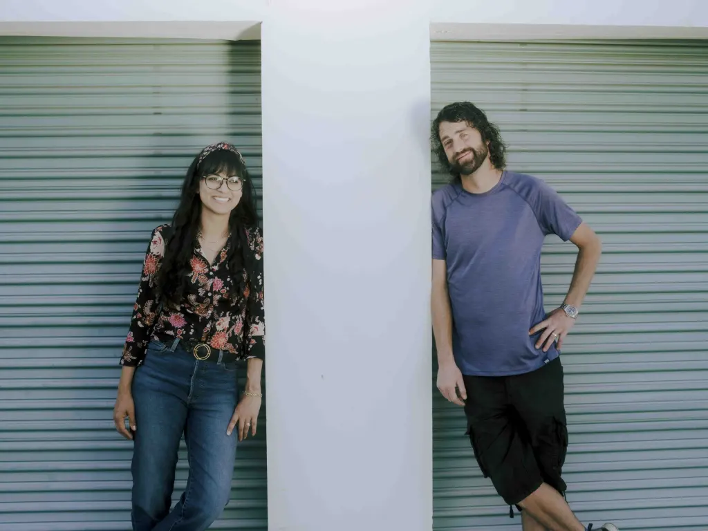 A man and a woman standing on opposite sides of a white pillar, smiling at the camera.