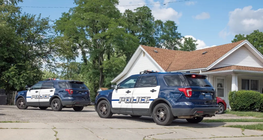 Two police cruisers parked in front of a white house.