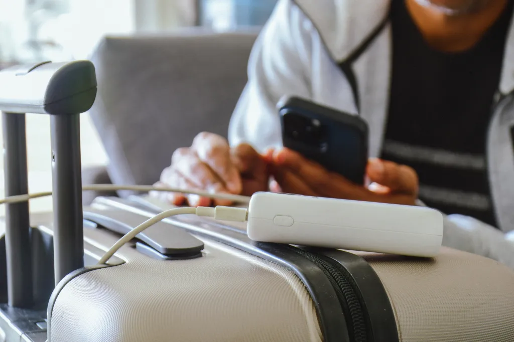 A man charges his phone with a power bank on his luggage in an airport lounge.