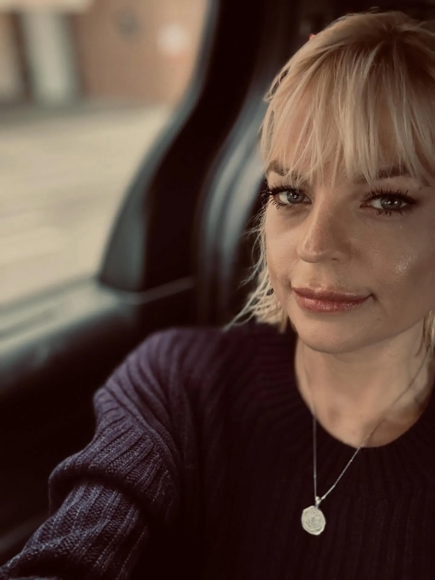 A woman with blonde bangs and a dark sweater looks at the camera.