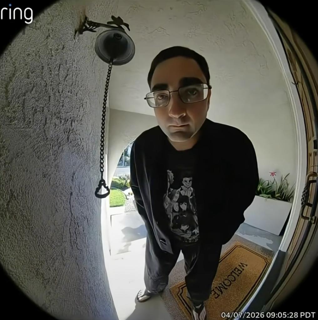 A man in glasses, a black sweatshirt, and dark pants, stands on a