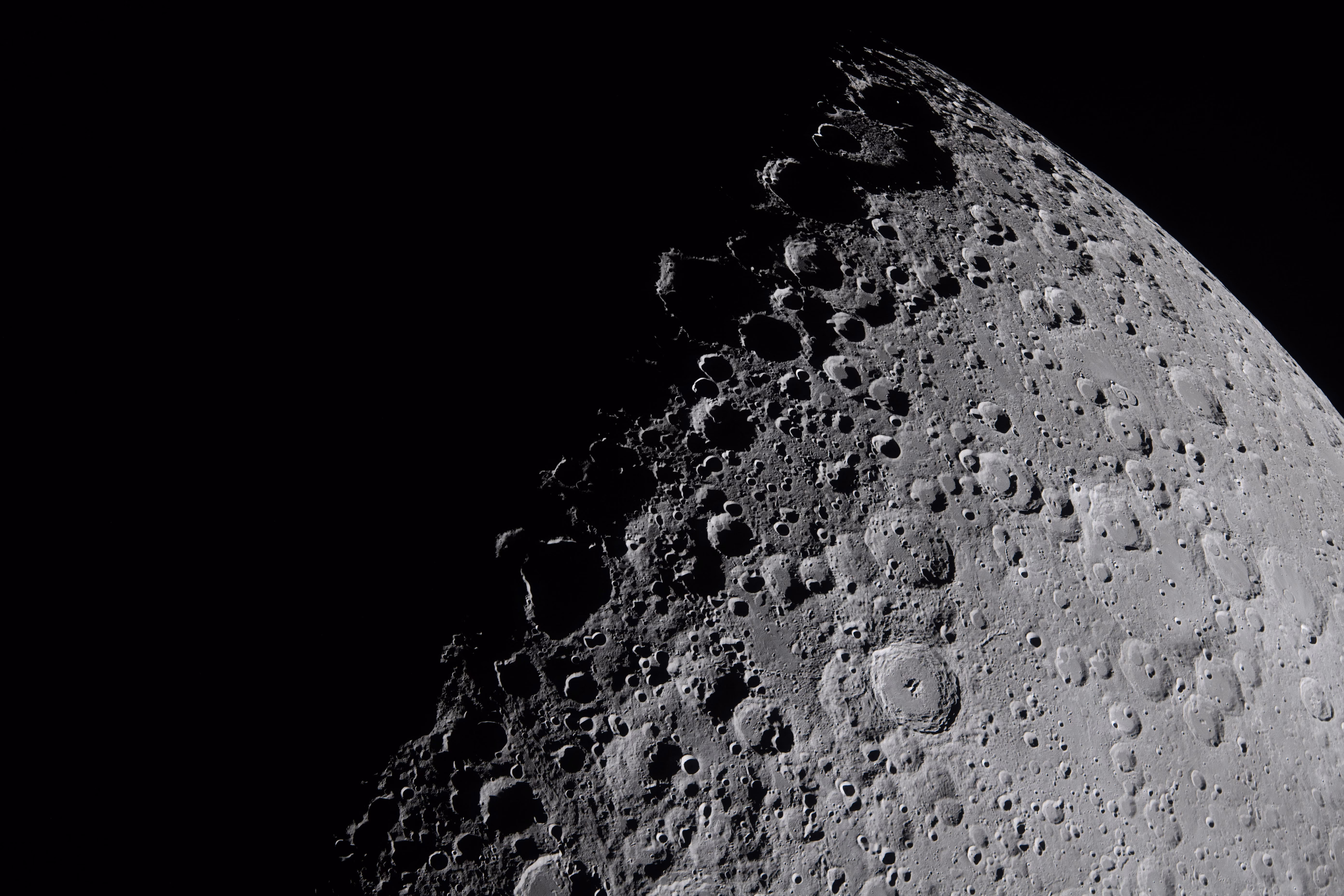 A close view of the surface of the moon, with many visible rugged craters along the line between shadow and sunlight