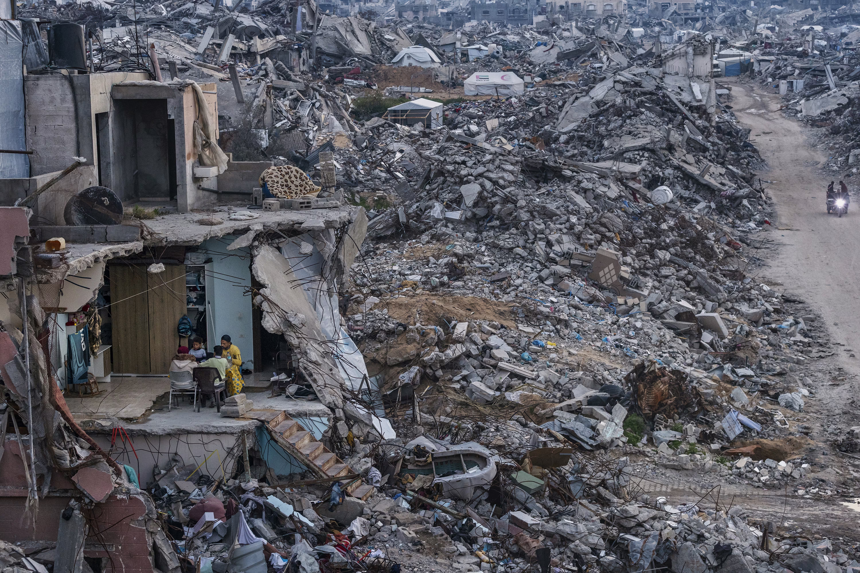 A family shares a meal in the remains of a destroyed building, situated among immense piles of rubble from other buildings in Gaza.
