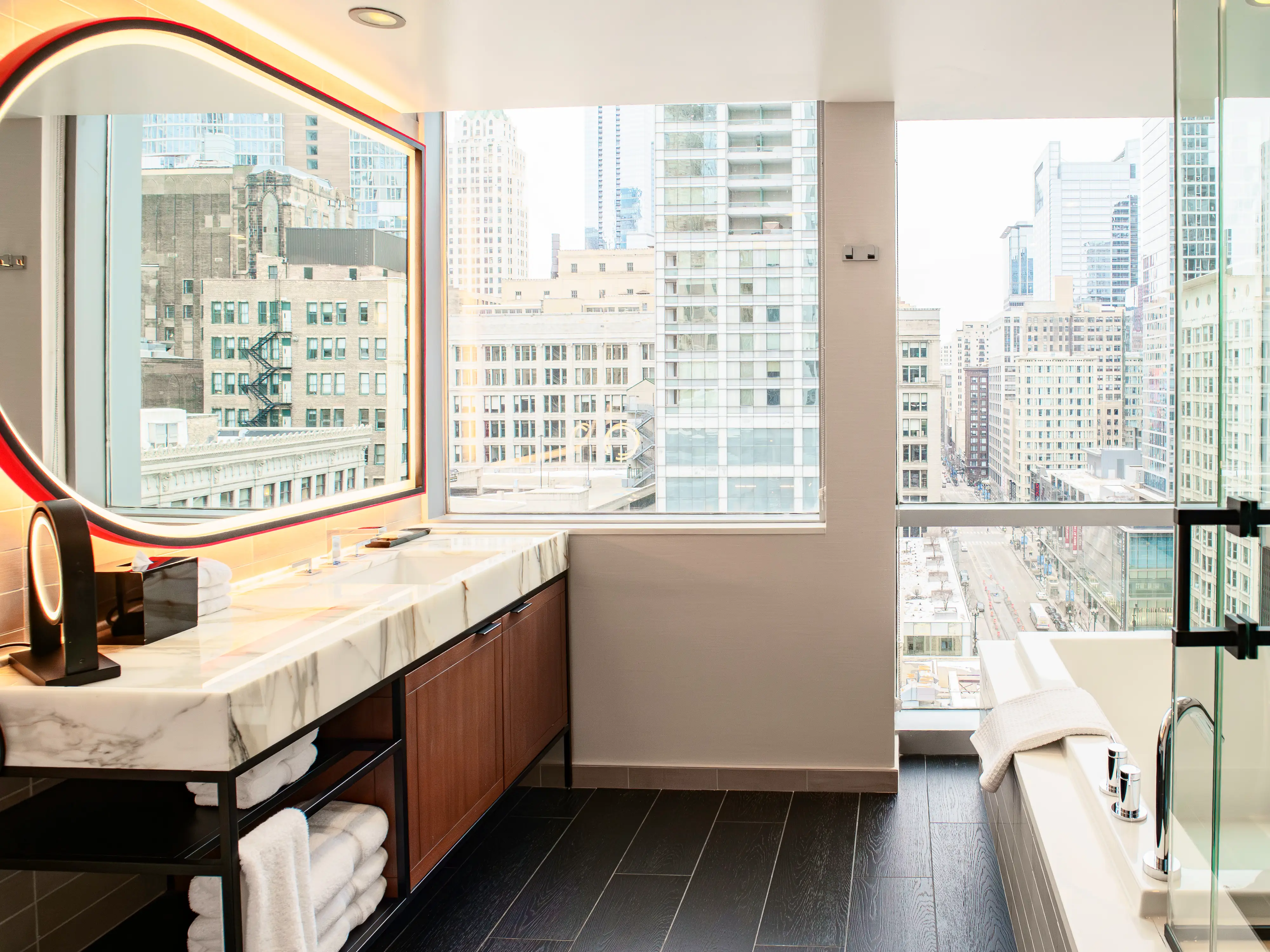 Inside a hotel bathroom with a vanity on the left, a shower and tub on the right, and wide windows on the back wall