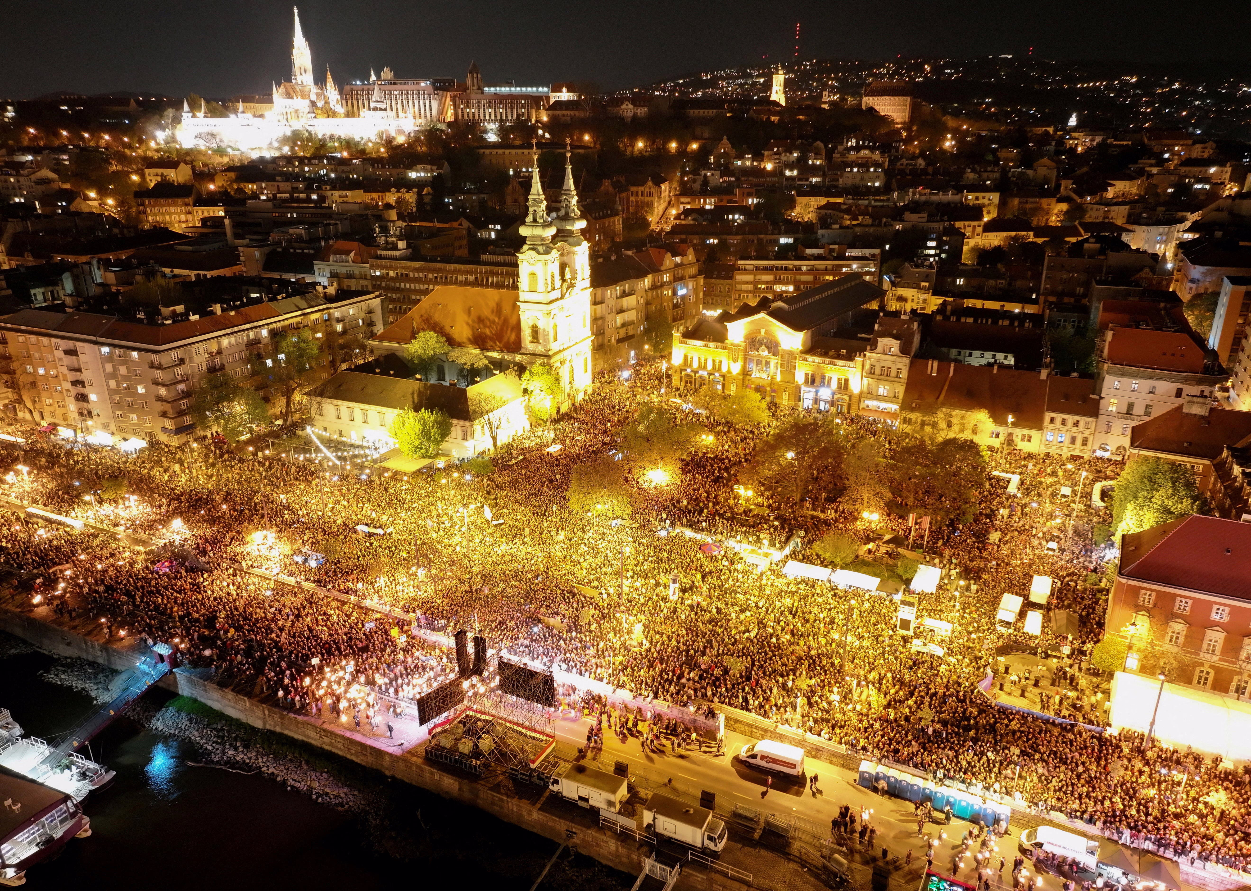 A drone view of a large crowd gathering to celebrate alongside the River Danube in Budapest, at night.