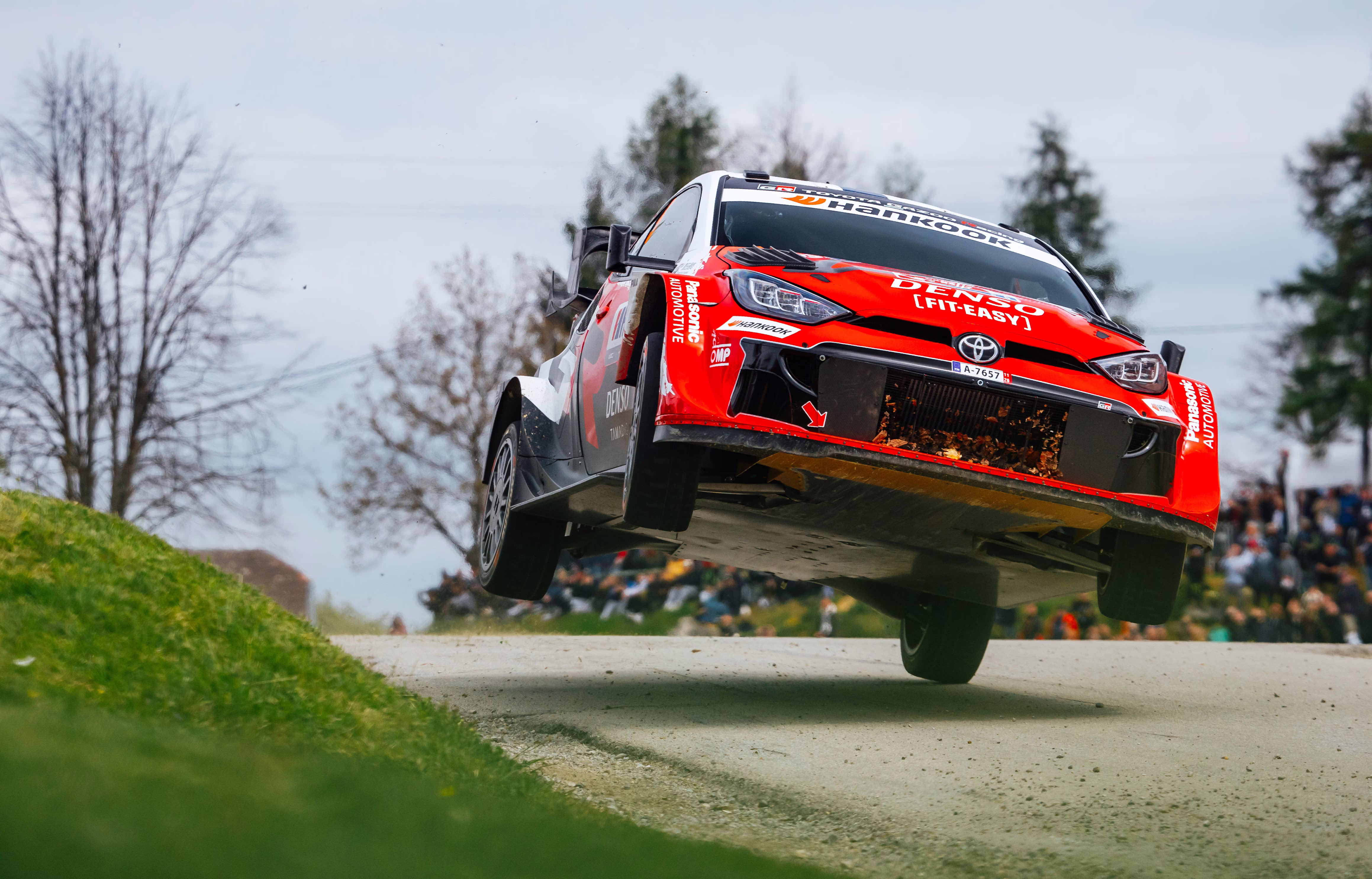 A rally car catches air while taking a corner, with only its left rear tire touching the pavement during a race.