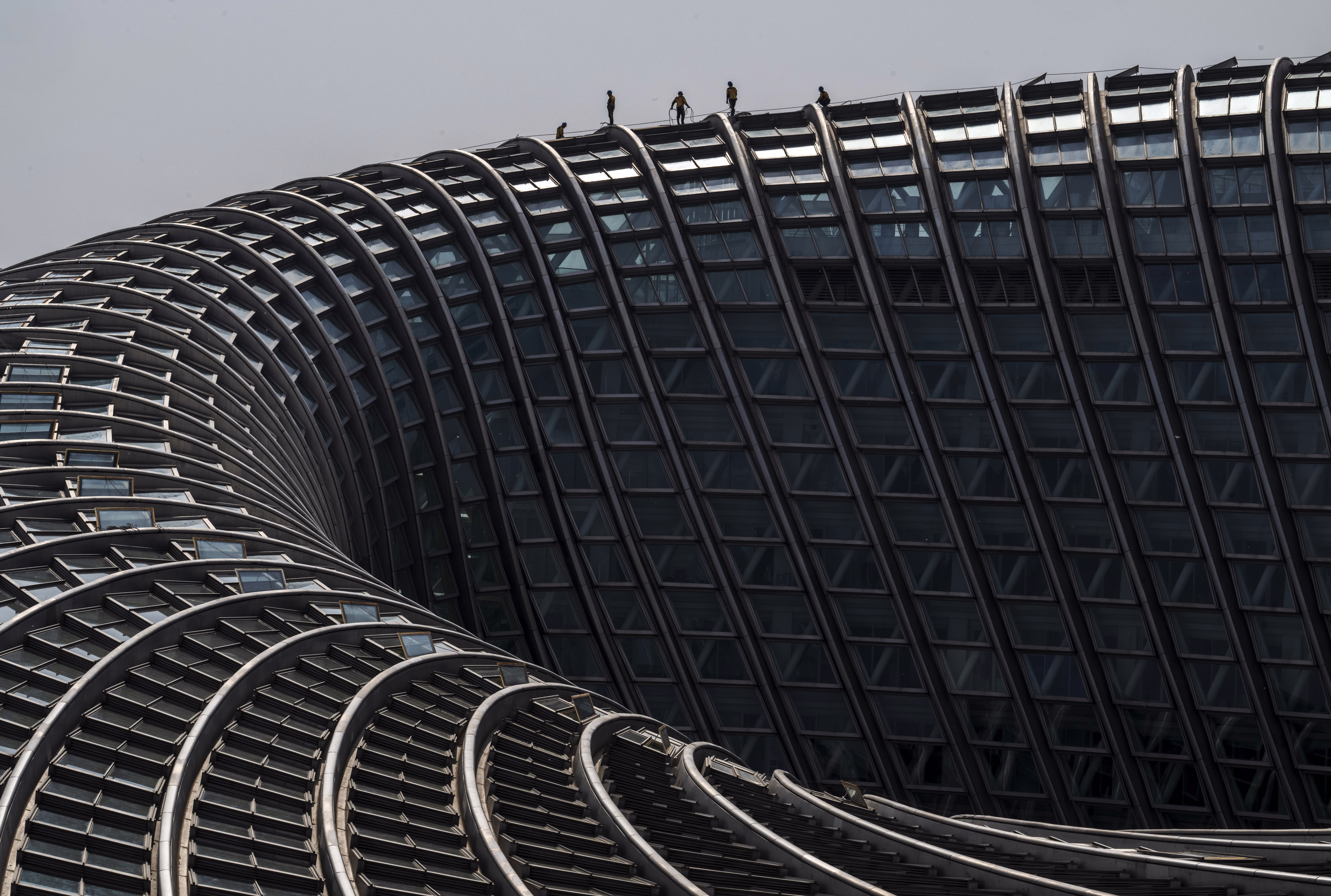 Workers stand on the roof of a large torus-shaped building.