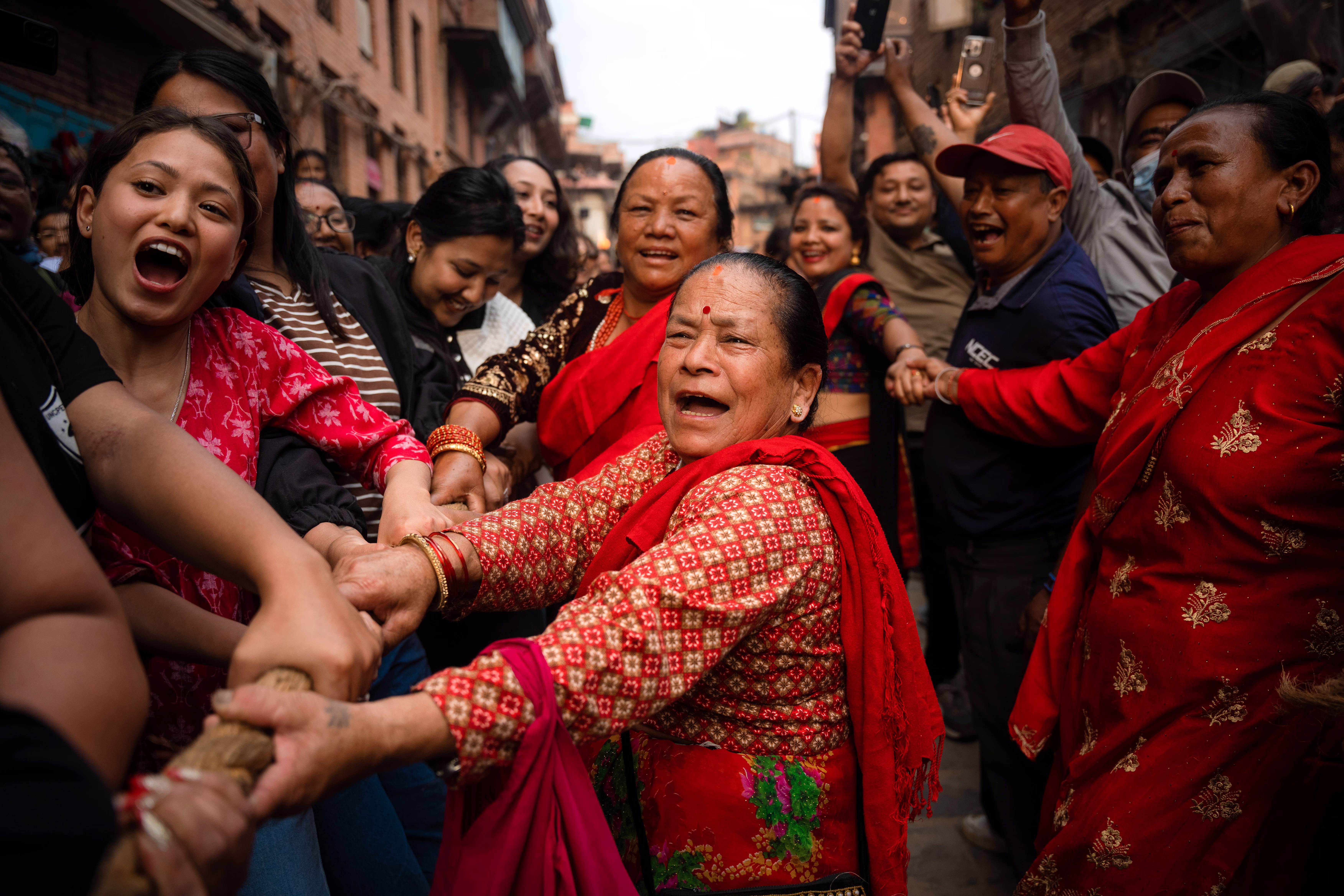 A group of people in a street cheer and pull on a rope attached to a chariot during a festival in Nepal.