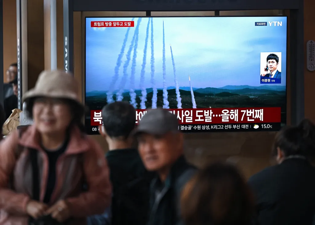 People watching a news broadcast on a large screen displaying footage of multiple North Korean missiles being launched.