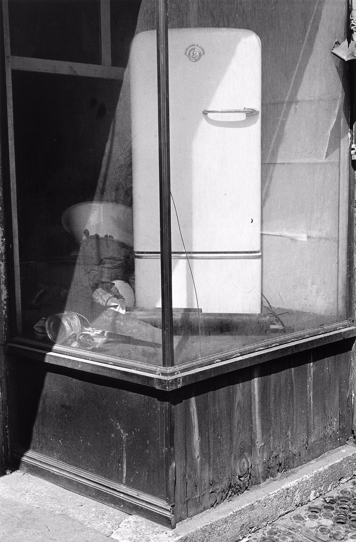 black-and-white photo of abandoned retail window with white refrigerator displayed