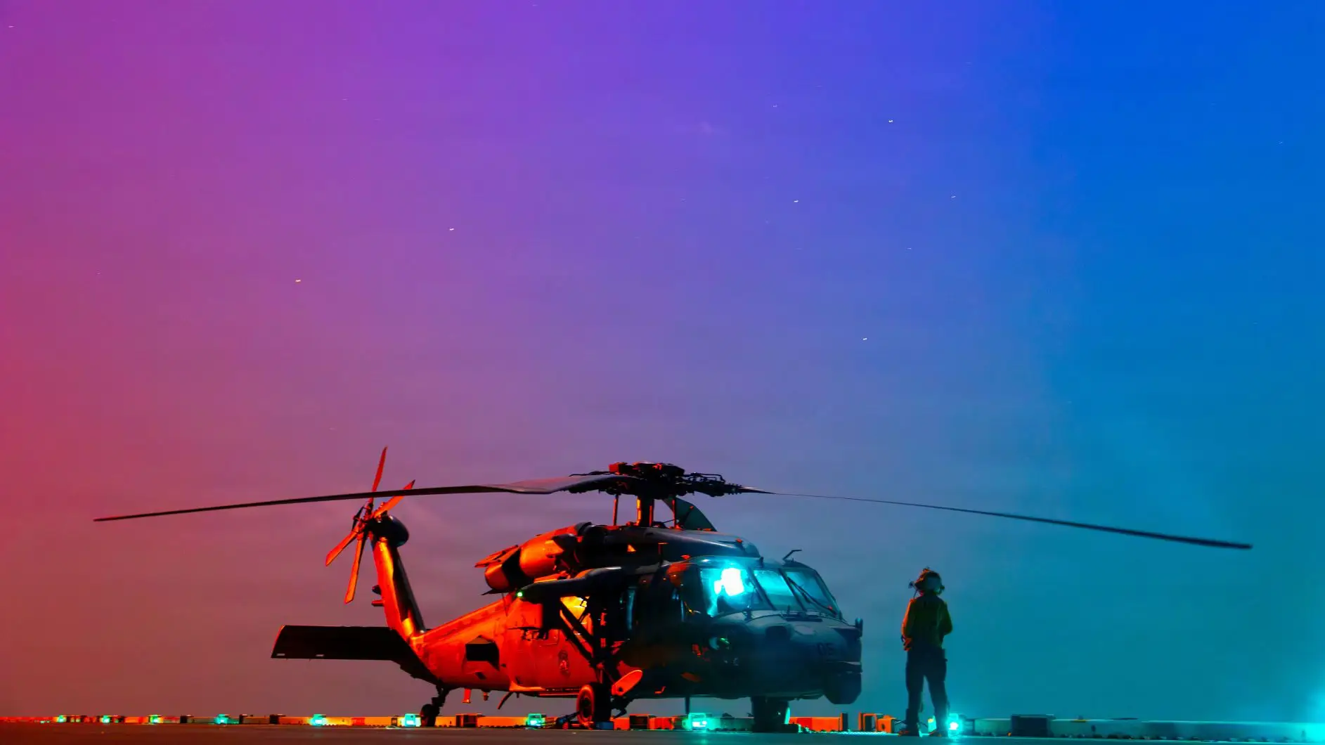 A helicopter sits on the deck of a ship with a colorful sky in the background.