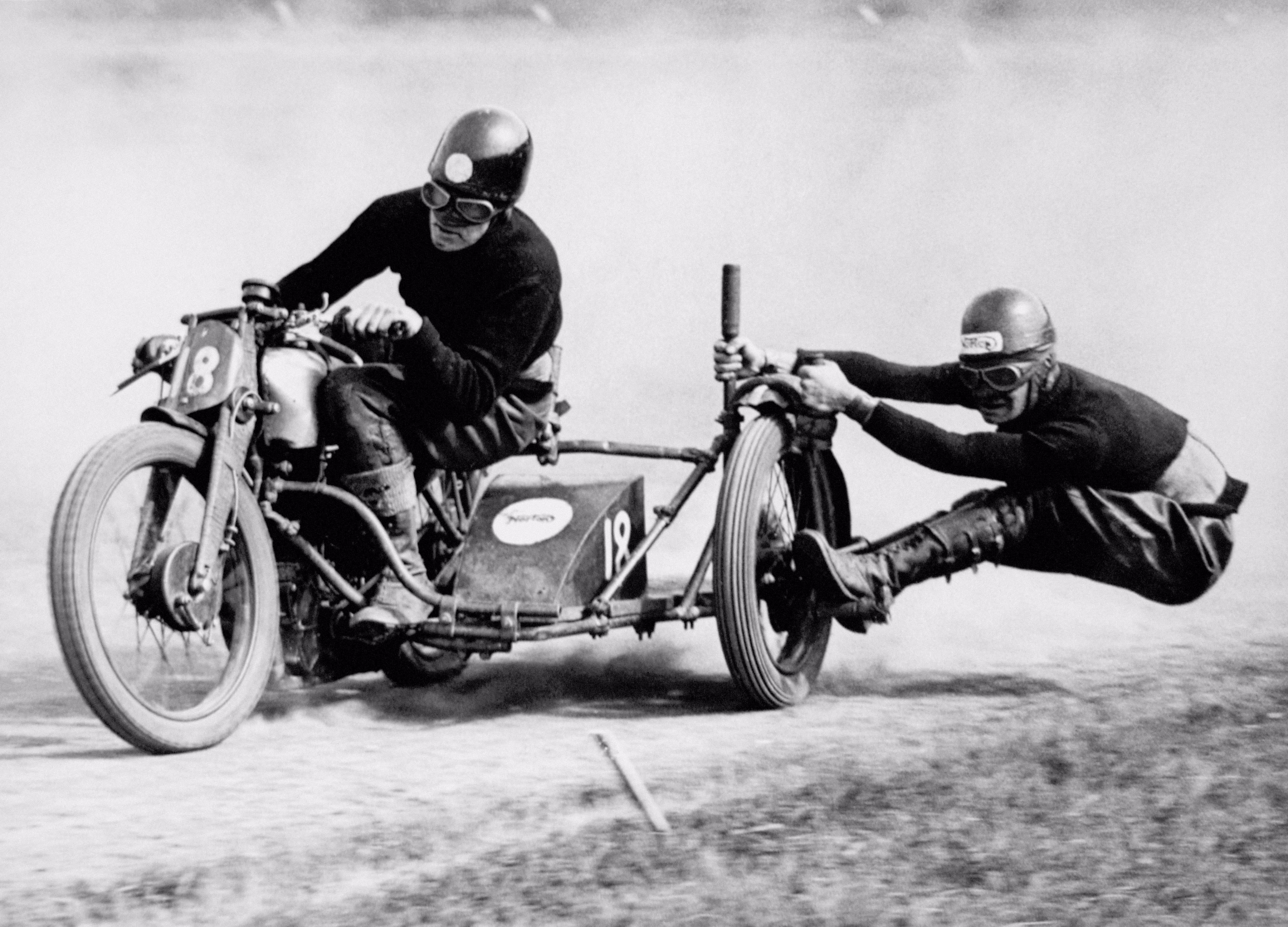 A 1936 photograph of a motorcycle racer with his sidecar passenger hanging off the outside of the far wheel during a sharp turn.
