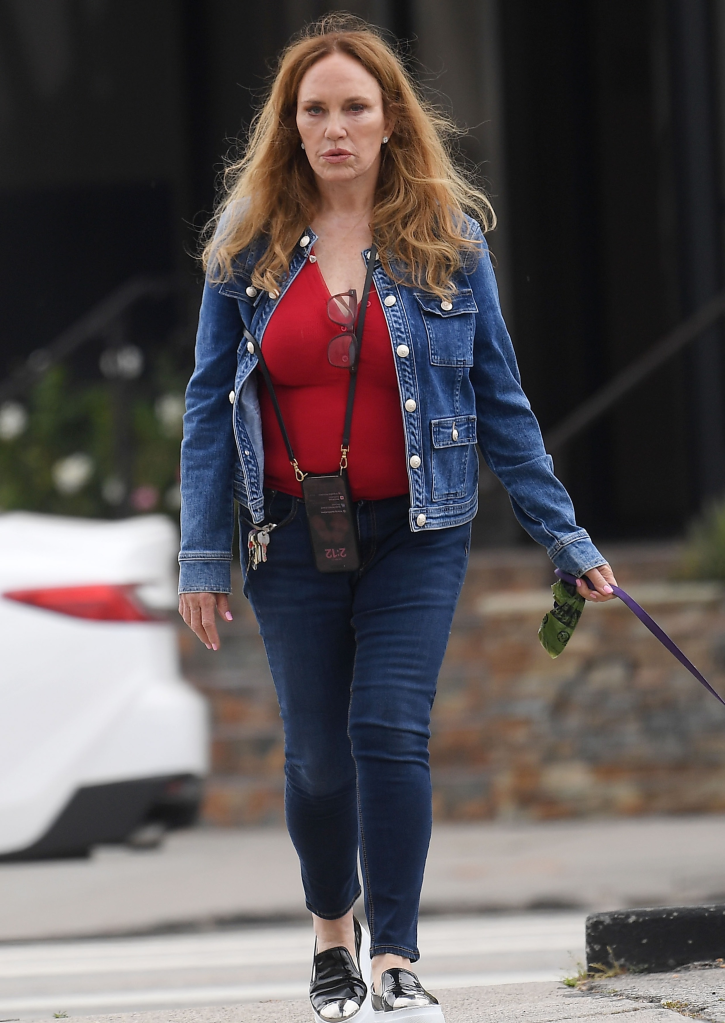 Catherine Bach wearing a red top, blue denim jacket, and blue jeans, holding a dog leash.