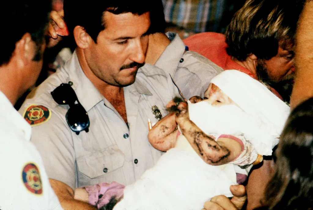 Jessica McClure, wrapped in white blankets with scrapes and bruises, being carried by a rescuer.