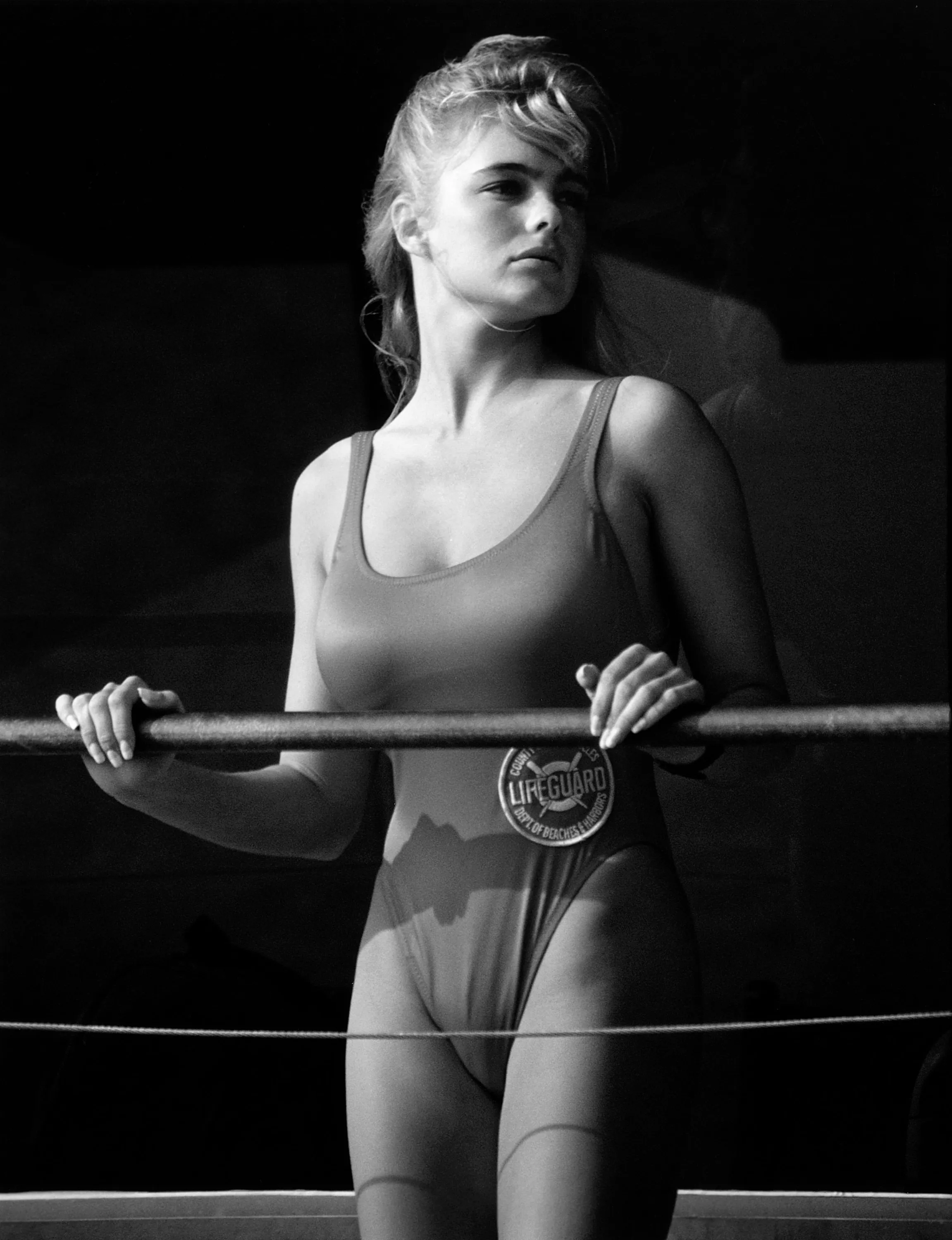 Erika Eleniak as a lifeguard in a swimsuit, holding onto a rail.