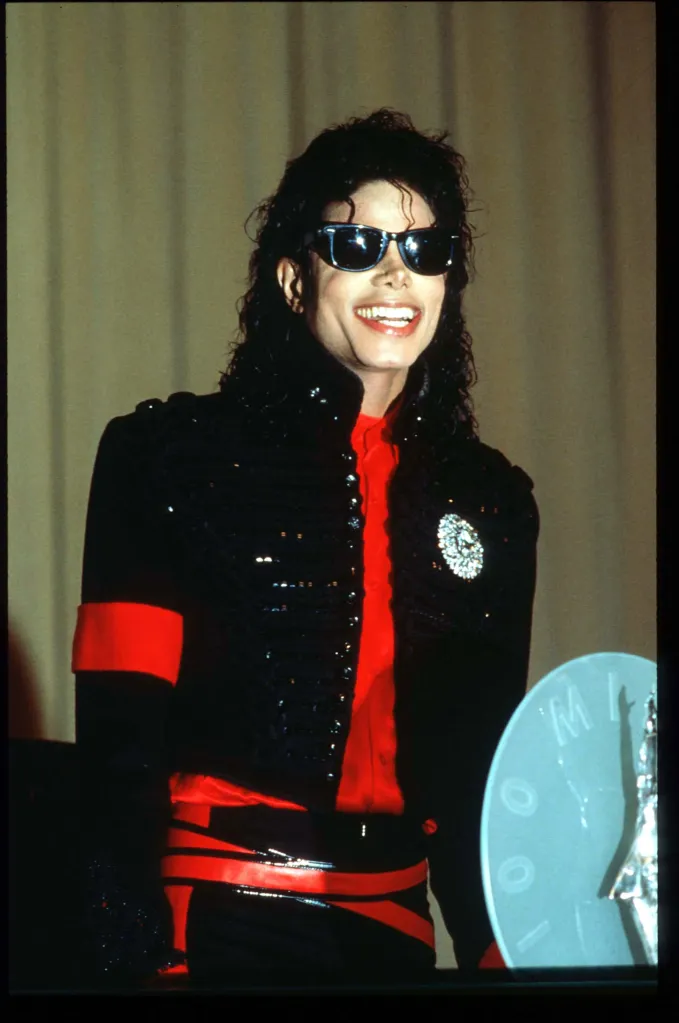 Michael Jackson smiling in sunglasses and a black and red uniform at a CBS Records award ceremony.